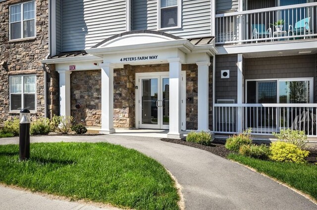 view of exterior entry featuring french doors, a balcony, and stone siding