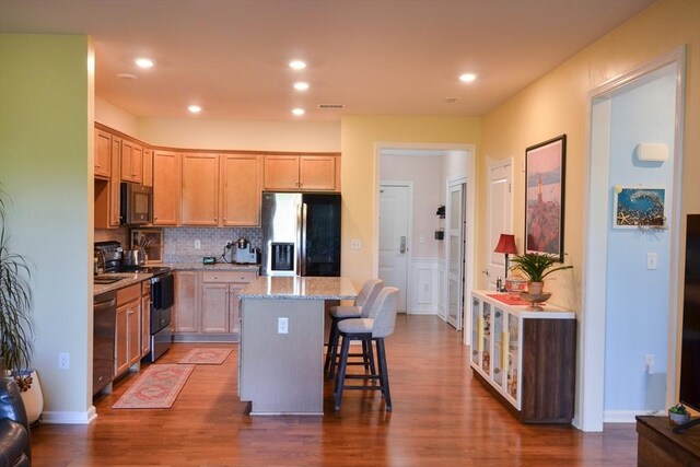 kitchen with dark wood-style flooring, appliances with stainless steel finishes, a breakfast bar area, a center island, and decorative backsplash