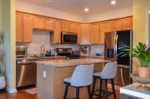 kitchen with appliances with stainless steel finishes, light stone counters, a sink, a kitchen breakfast bar, and tasteful backsplash