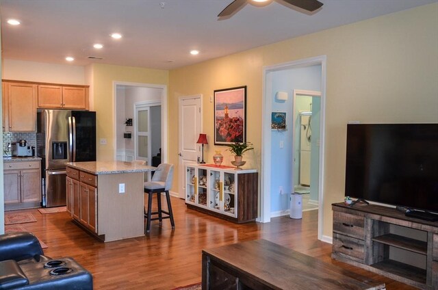 kitchen with ceiling fan, a center island, a kitchen bar, stainless steel refrigerator with ice dispenser, and dark wood-type flooring