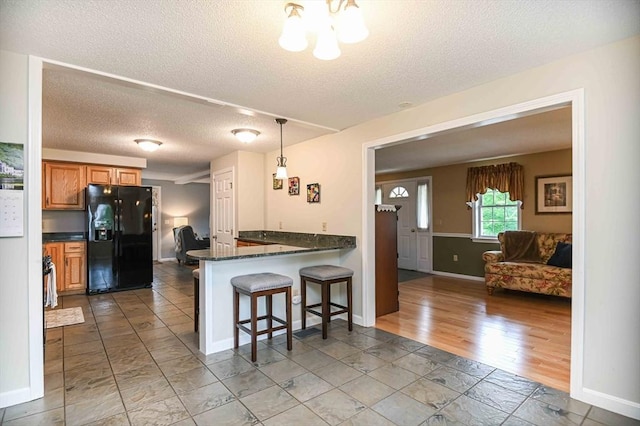 20 Bowdoin Dr, Haverhill, MA 01830 - kitchen featuring black fridge with ice dispenser, a textured ceiling, a kitchen breakfast bar, brown cabinetry, and a peninsula
