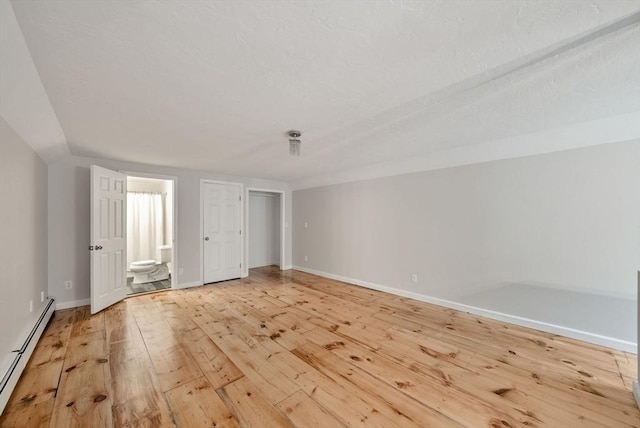 176 Spring St, Hopkinton, MA 01748 - unfurnished bedroom with baseboard heating, light wood-style floors, baseboards, and connected bathroom