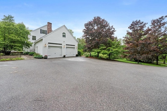176 Spring St, Hopkinton, MA 01748 - view of side of home with a garage, asphalt driveway, and a chimney