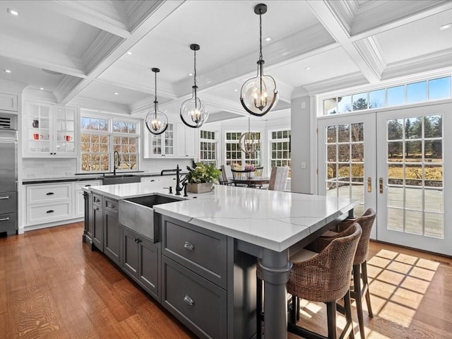 kitchen with french doors, beam ceiling, a large island, white cabinets, and a sink