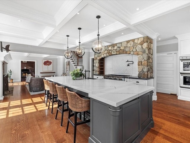 kitchen featuring light stone counters, dark wood-style flooring, coffered ceiling, and beamed ceiling