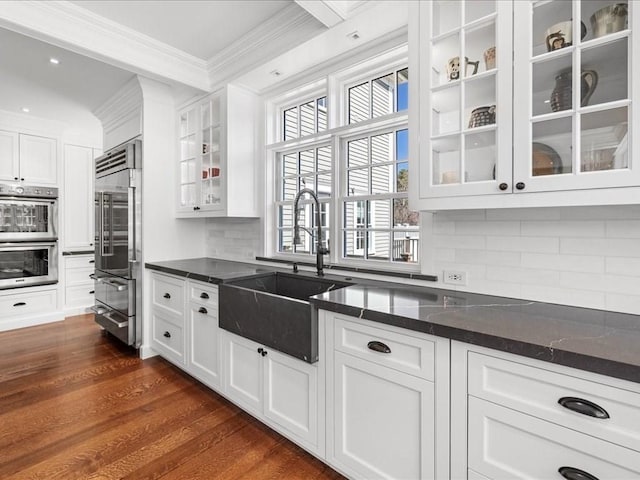 kitchen with appliances with stainless steel finishes, dark wood-type flooring, ornamental molding, white cabinets, and a sink