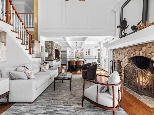 living area featuring a stone fireplace, coffered ceiling, wood finished floors, stairs, and beam ceiling