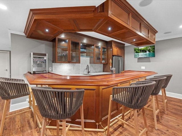 bar featuring indoor wet bar, decorative backsplash, light wood-style floors, freestanding refrigerator, and a sink