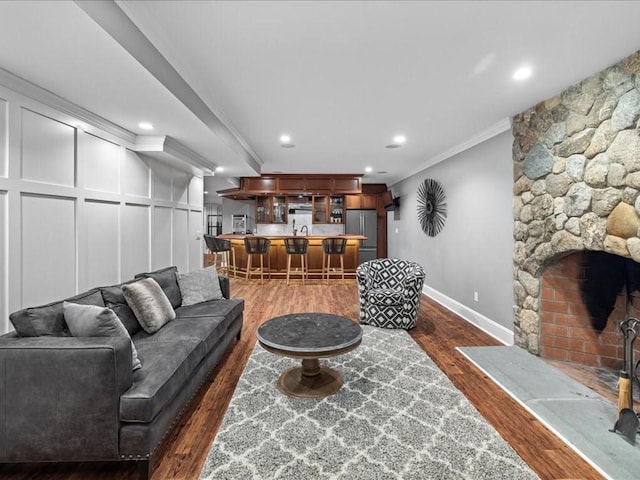 living room featuring recessed lighting, ornamental molding, a stone fireplace, wood finished floors, and baseboards