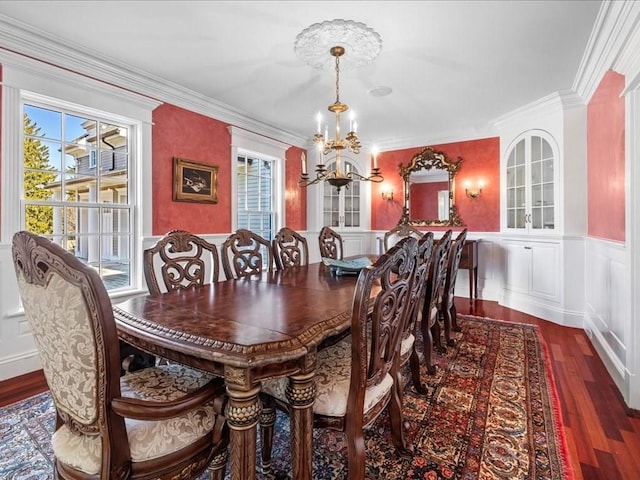 dining space with wainscoting, wood finished floors, crown molding, a chandelier, and a decorative wall