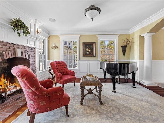 living area featuring a wainscoted wall, a fireplace, ornate columns, and wood finished floors