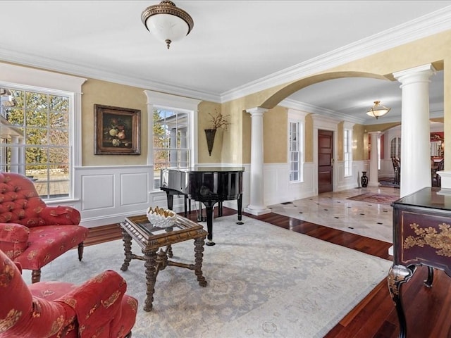 sitting room featuring arched walkways, wainscoting, ornate columns, and wood finished floors