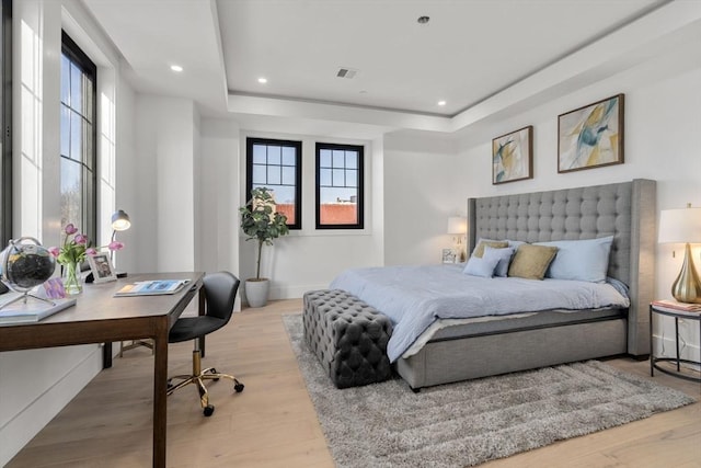 bedroom with a tray ceiling, multiple windows, and light wood-type flooring