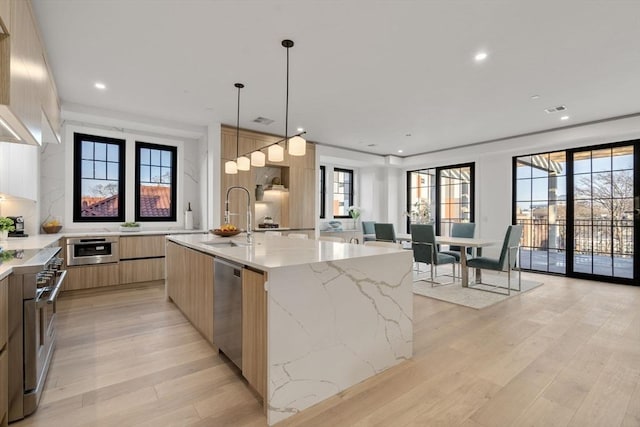 kitchen with sink, light stone counters, hanging light fixtures, a large island with sink, and stainless steel appliances