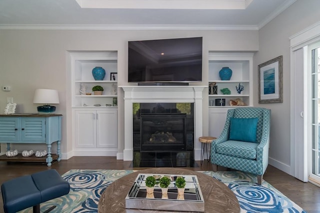 living area featuring wood finished floors, ornamental molding, a fireplace, built in shelves, and baseboards
