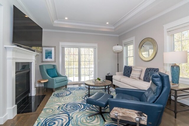 living area with a fireplace with flush hearth, a tray ceiling, wood finished floors, and crown molding