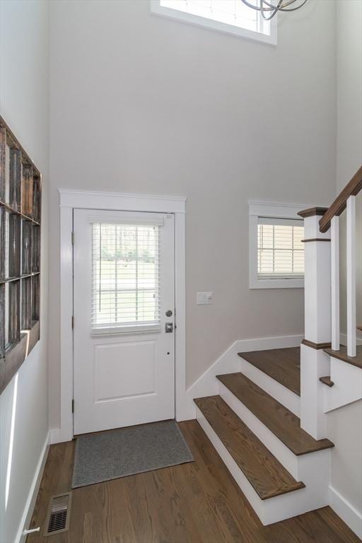 doorway featuring a towering ceiling, stairs, plenty of natural light, and wood finished floors