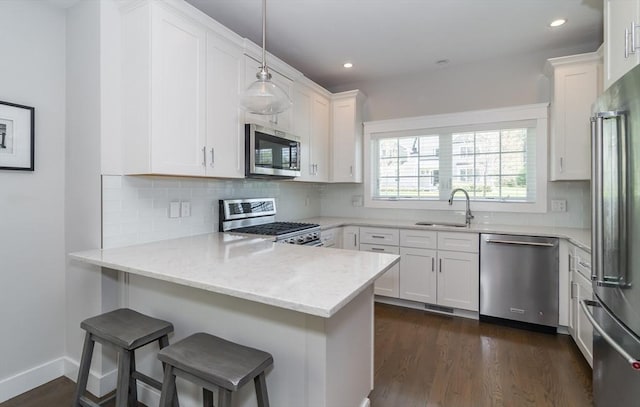 kitchen featuring stainless steel appliances, a sink, a peninsula, white cabinets, and recessed lighting