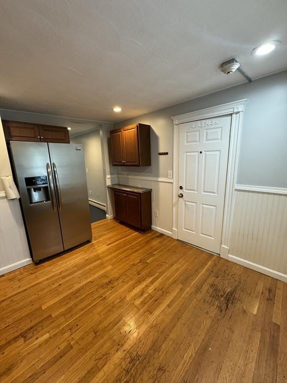 kitchen with dark brown cabinetry, light hardwood / wood-style flooring, and stainless steel refrigerator with ice dispenser