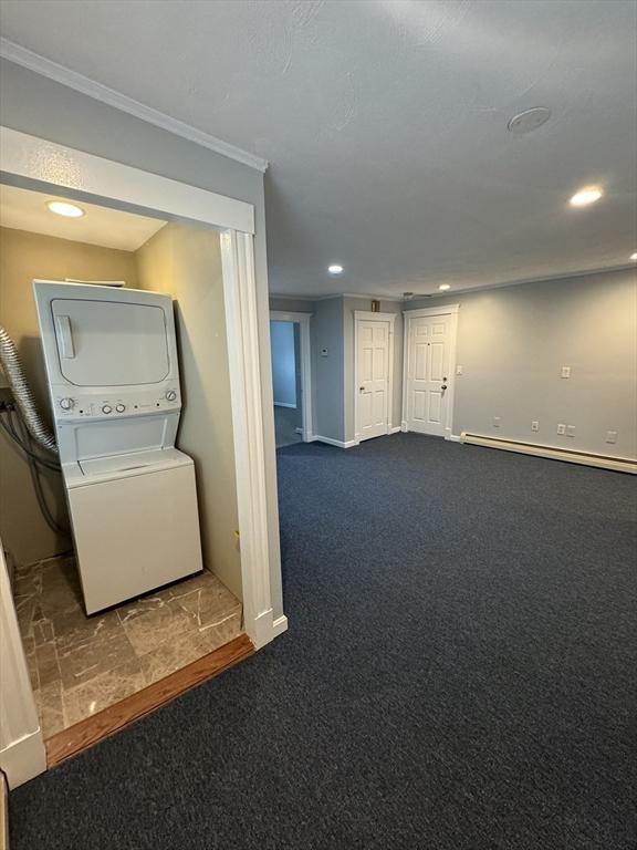 interior space featuring dark colored carpet, ornamental molding, baseboard heating, and stacked washer / drying machine