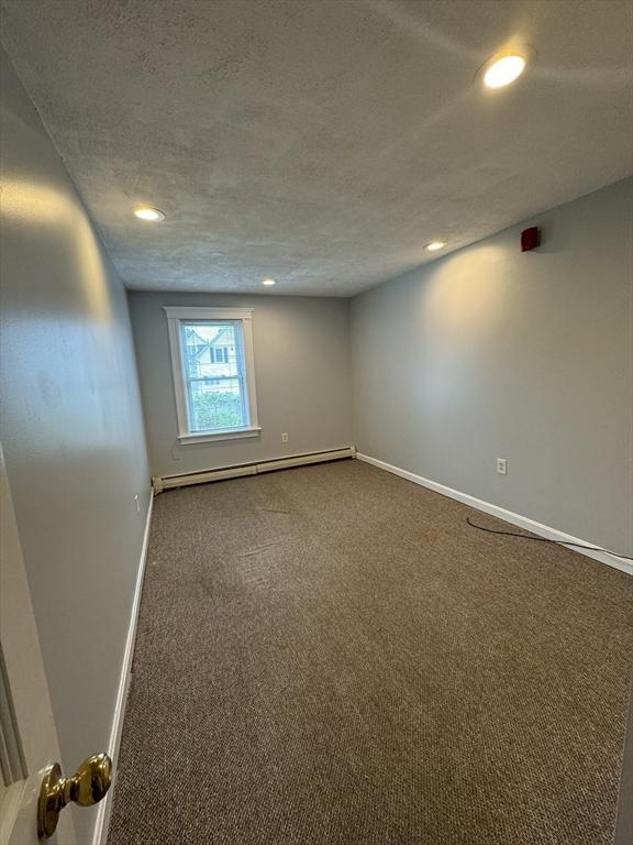 empty room with baseboard heating, carpet flooring, and a textured ceiling