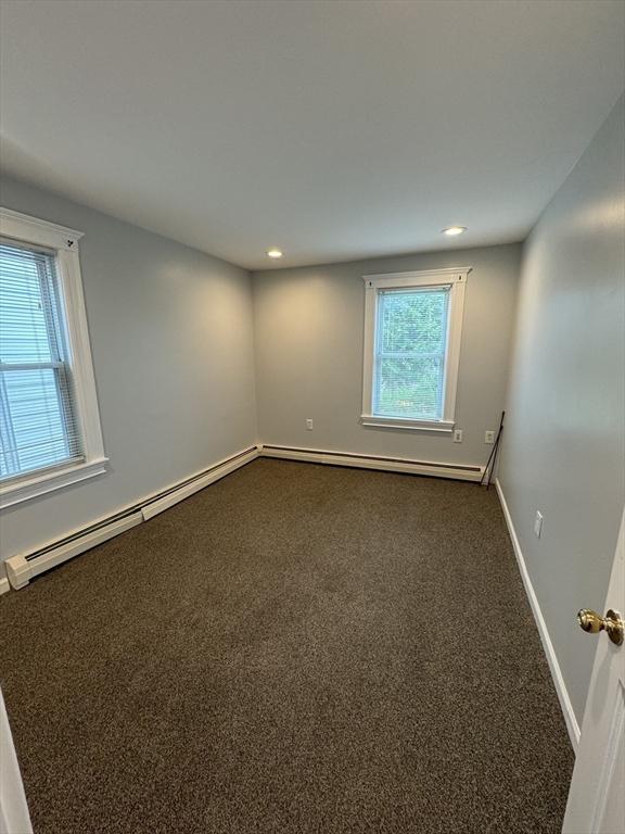 spare room with dark colored carpet and a baseboard radiator