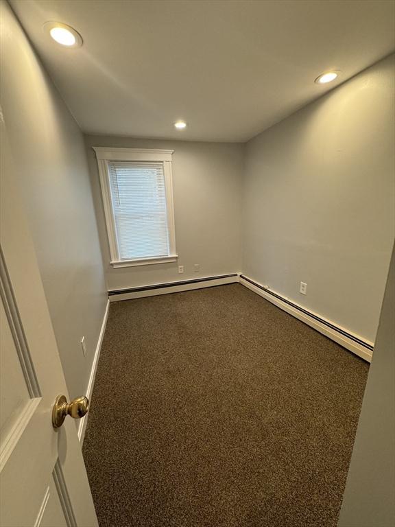 carpeted empty room with a baseboard heating unit