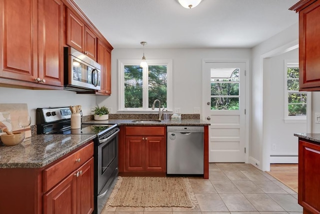 kitchen featuring light tile patterned flooring, baseboard heating, a sink, dark stone counters, and stainless steel appliances