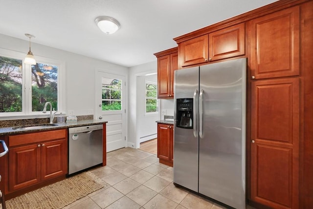 kitchen featuring brown cabinets, a sink, dark stone countertops, stainless steel appliances, and light tile patterned floors