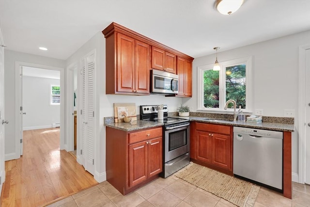 kitchen with a sink, dark stone counters, stainless steel appliances, and brown cabinets