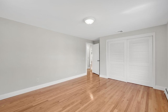 unfurnished bedroom featuring light wood-style floors, baseboards, a baseboard radiator, visible vents, and a closet