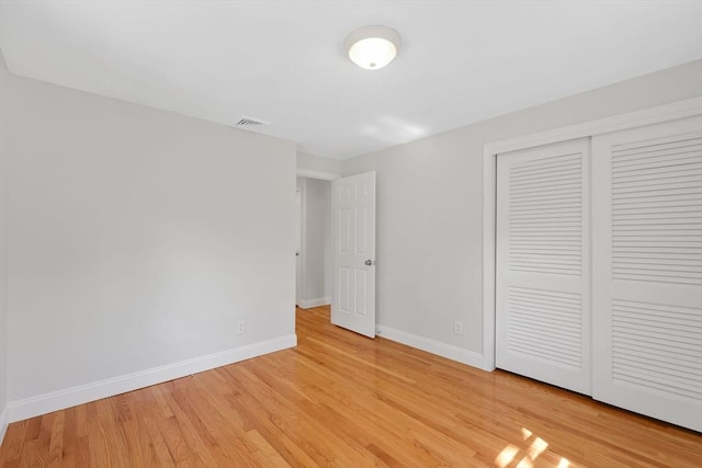 unfurnished bedroom featuring baseboards, light wood-style flooring, visible vents, and a closet