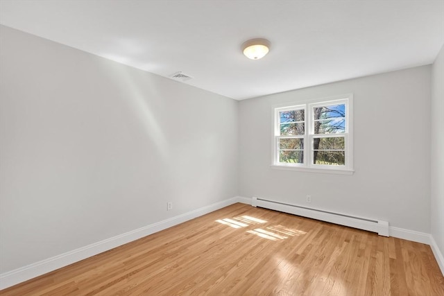 empty room with baseboards, light wood finished floors, a baseboard heating unit, and visible vents