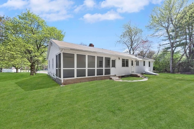 back of property featuring a sunroom, a chimney, and a yard