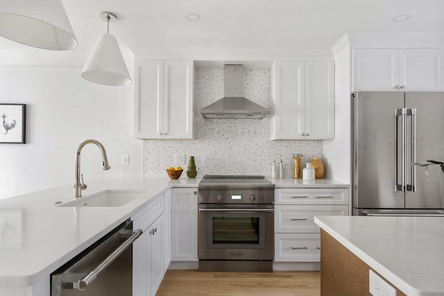 kitchen with decorative light fixtures, wall chimney range hood, sink, white cabinetry, and premium appliances
