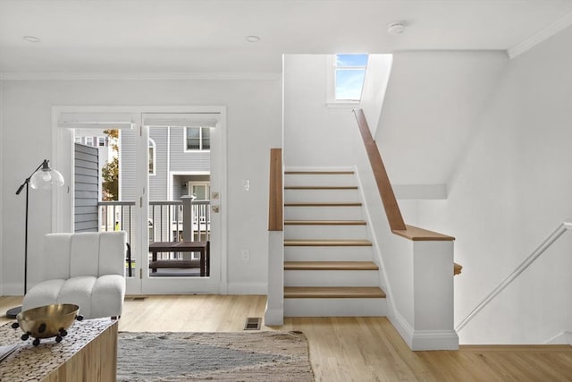 stairs with wood-type flooring, a wealth of natural light, ornamental molding, and a skylight