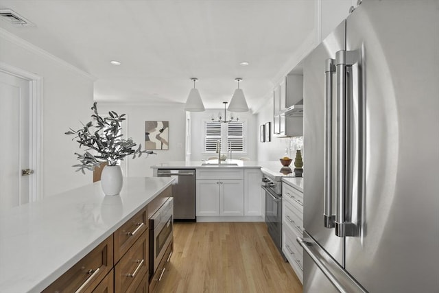 kitchen with sink, white cabinetry, hanging light fixtures, light wood-type flooring, and premium appliances