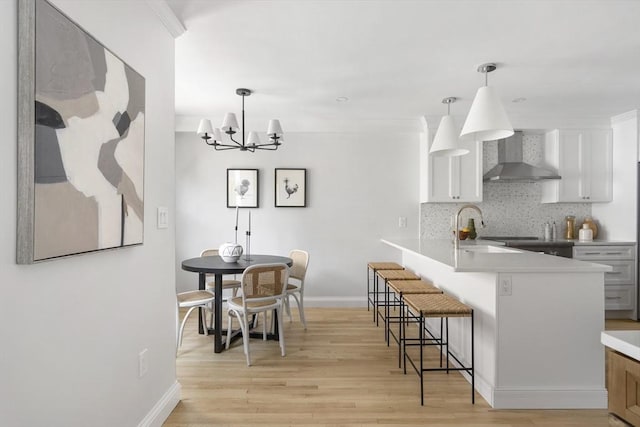 kitchen featuring decorative light fixtures, wall chimney exhaust hood, tasteful backsplash, and white cabinetry