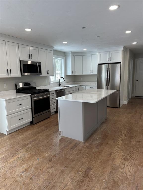 kitchen with sink, white cabinetry, a kitchen island, hardwood / wood-style flooring, and stainless steel appliances