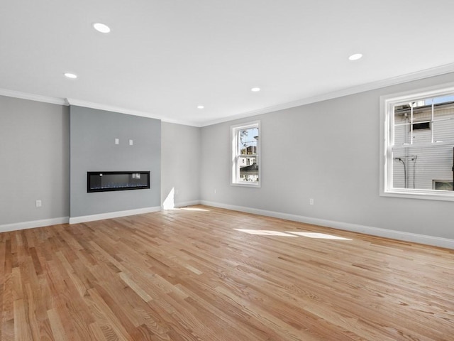 unfurnished living room featuring light wood-style flooring, recessed lighting, baseboards, ornamental molding, and a glass covered fireplace