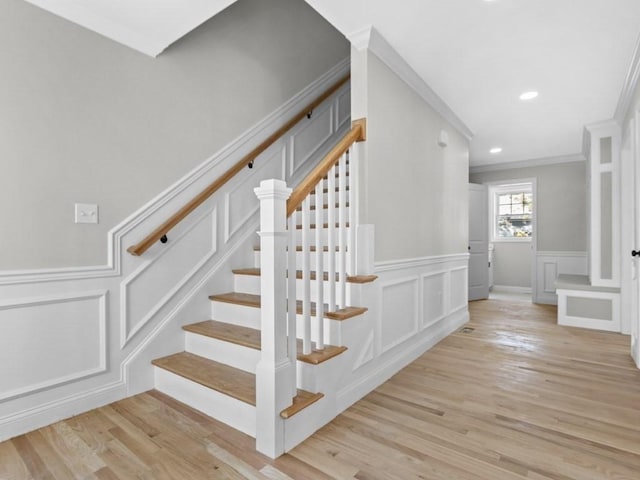 stairs with crown molding, a decorative wall, wood finished floors, and recessed lighting