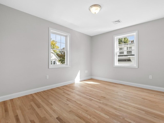 unfurnished room featuring light wood finished floors, visible vents, and baseboards