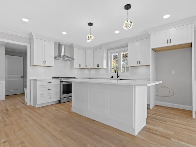 kitchen featuring light wood-style flooring, white cabinets, light countertops, wall chimney exhaust hood, and gas range