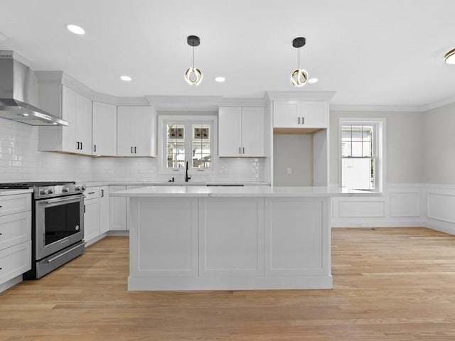 kitchen featuring light countertops, wall chimney range hood, stainless steel gas range, and white cabinets