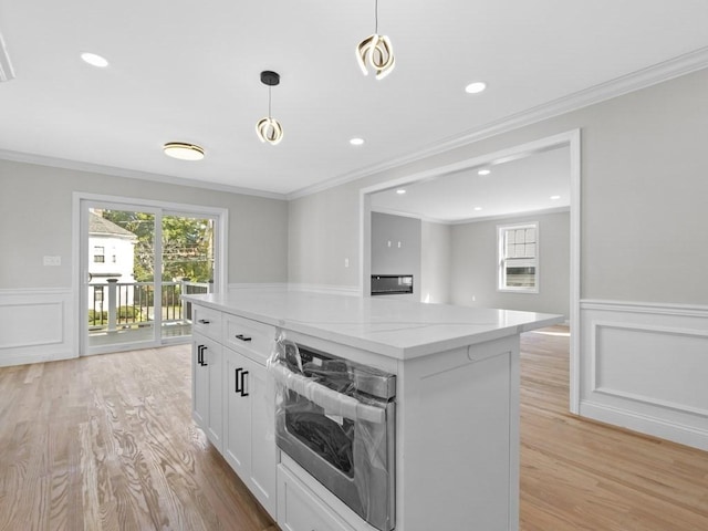 kitchen featuring oven, a kitchen island, white cabinetry, light wood-style floors, and light stone countertops