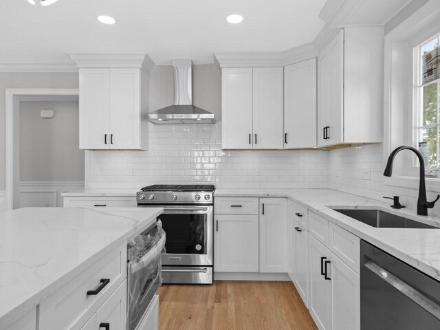 kitchen with stainless steel range with gas cooktop, light wood-style floors, a sink, wall chimney range hood, and dishwashing machine