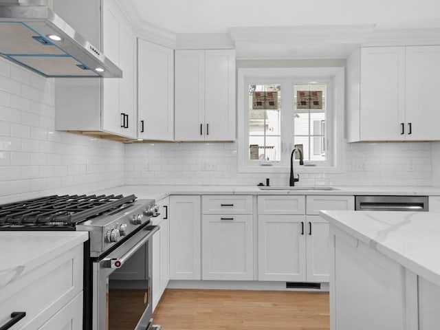 kitchen with gas stove, white cabinetry, a sink, wall chimney range hood, and light stone countertops