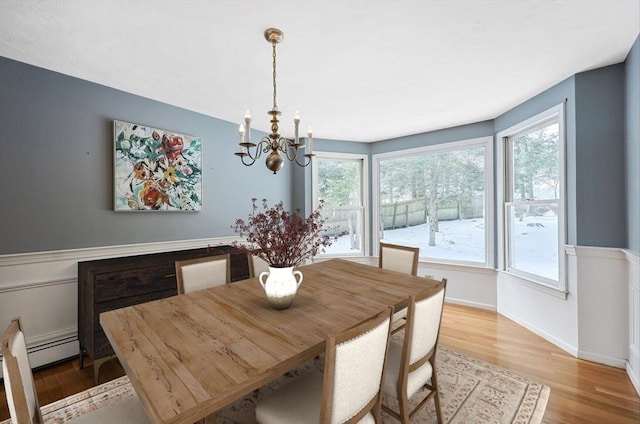 dining space featuring a wainscoted wall, light wood-style flooring, baseboards, and a notable chandelier