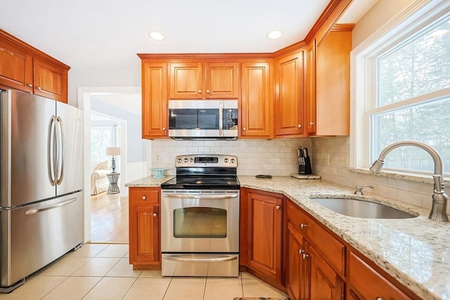 kitchen with light tile patterned floors, tasteful backsplash, appliances with stainless steel finishes, light stone counters, and a sink