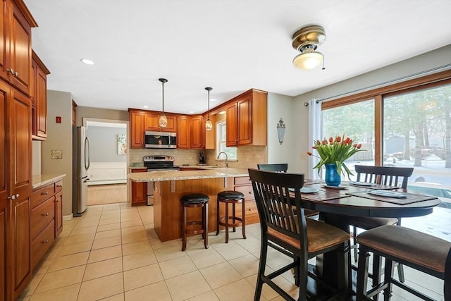 kitchen with light stone counters, stainless steel appliances, backsplash, brown cabinetry, and pendant lighting